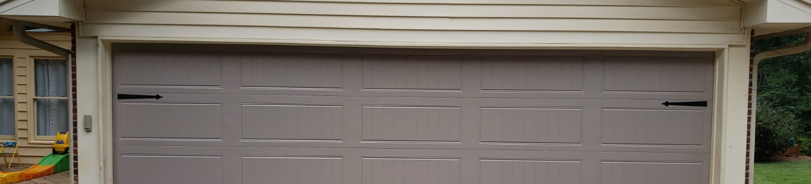 Newly installed beige steel garage door with decorative hardware on Irving, TX home